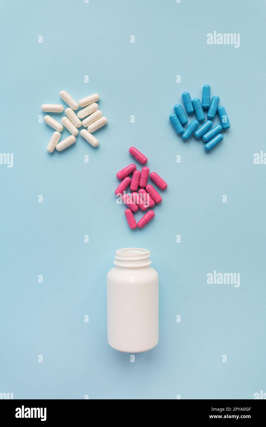 Verschiedene mehrfarbige helle Kapselpillen, die aus einer offenen Plastikflasche fliegen, isoliert auf blauem Hintergrund. Das Konzept der evidenzbasierten Medizin und des Gesundheitswesens. Stockfoto