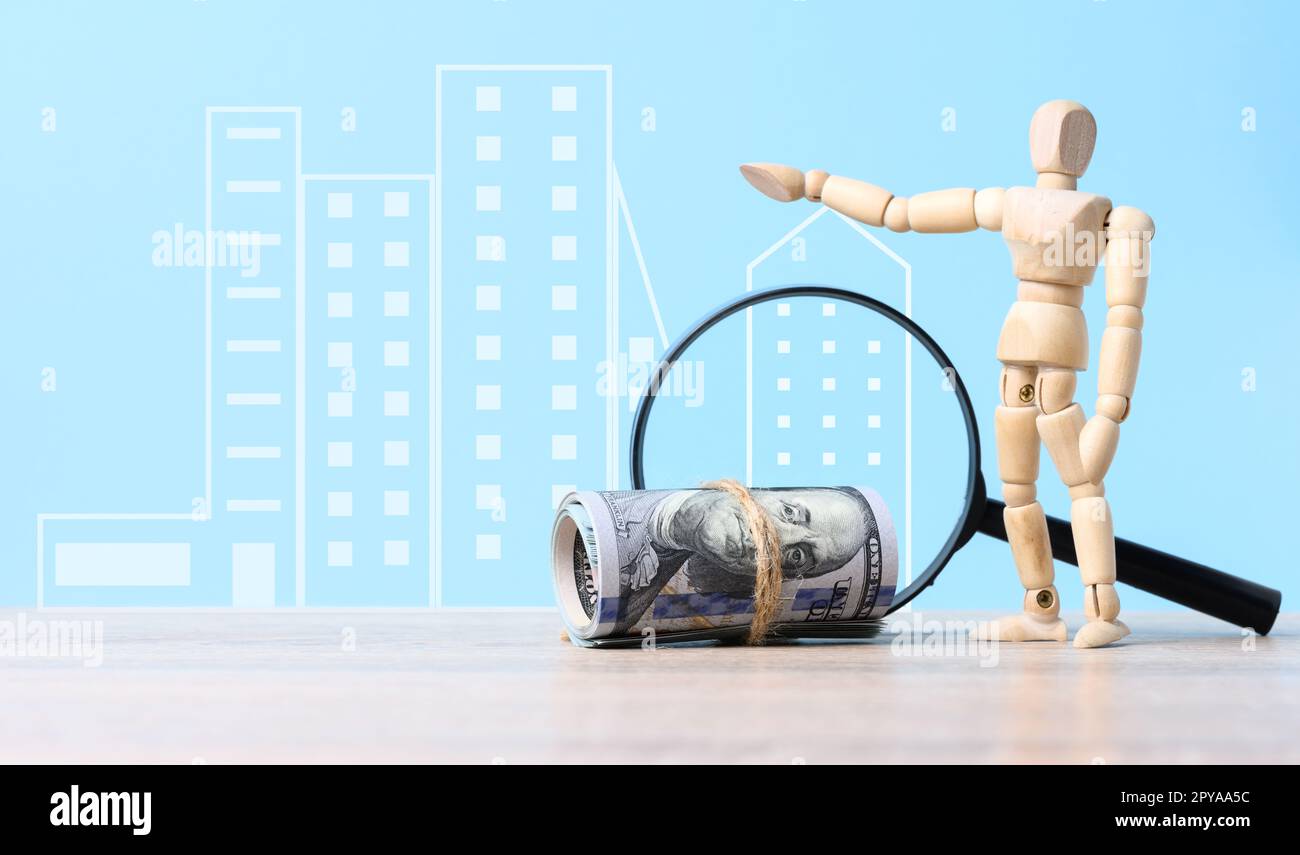 Ein Bündel Papierdollar, eine Lupe und eine hölzerne Marionettenpuppe auf blauem Hintergrund, ein Konzept steigender Immobilienpreise, hohe Hypothekenzinsen Stockfoto