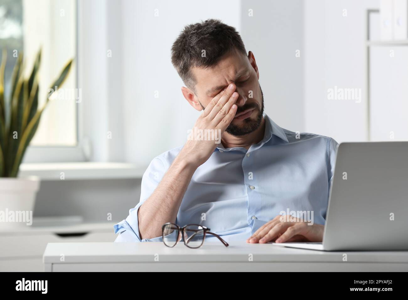 Ein Mann mit Augenschmerzen am Schreibtisch im Büro Stockfoto