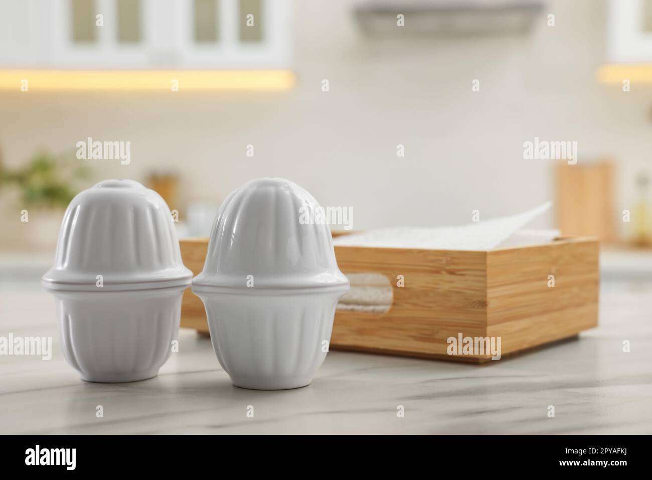 Keramiksalz- und Pfefferstreuer in der Nähe einer Serviettenschachtel auf einem weißen Marmortisch in der Küche. Platz für Text Stockfoto
