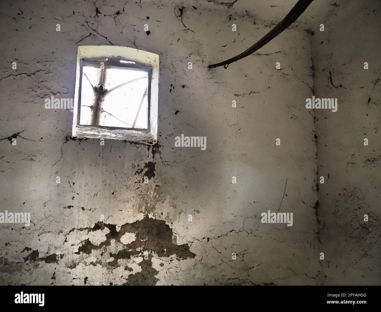 Ein kleines Fenster oben an der Wand. Gruselige Wände mit Spinnweben. Ein alter Kirchenwohnheim. Halloween oder Spukort. Gefängniszelle mit Folterseilen. Visionen und eine Welt voller Halluzinationen Stockfoto