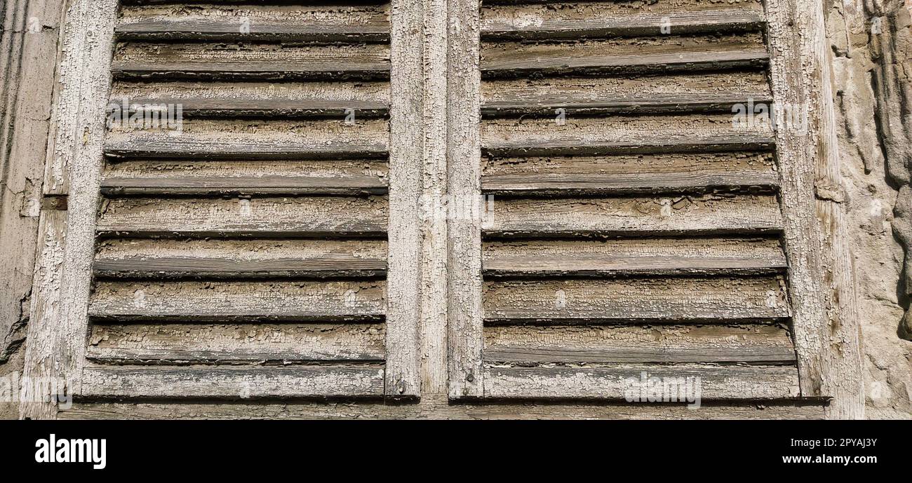 Alte Holzläden am Fenster. Antike Holzarchitektur. Trockenes Holz mit rostender, verfärbter Farbe. Schalen und Staub. Natürliche Farbe. Fensterbank, horizontale Streifen und Leisten. Stockfoto