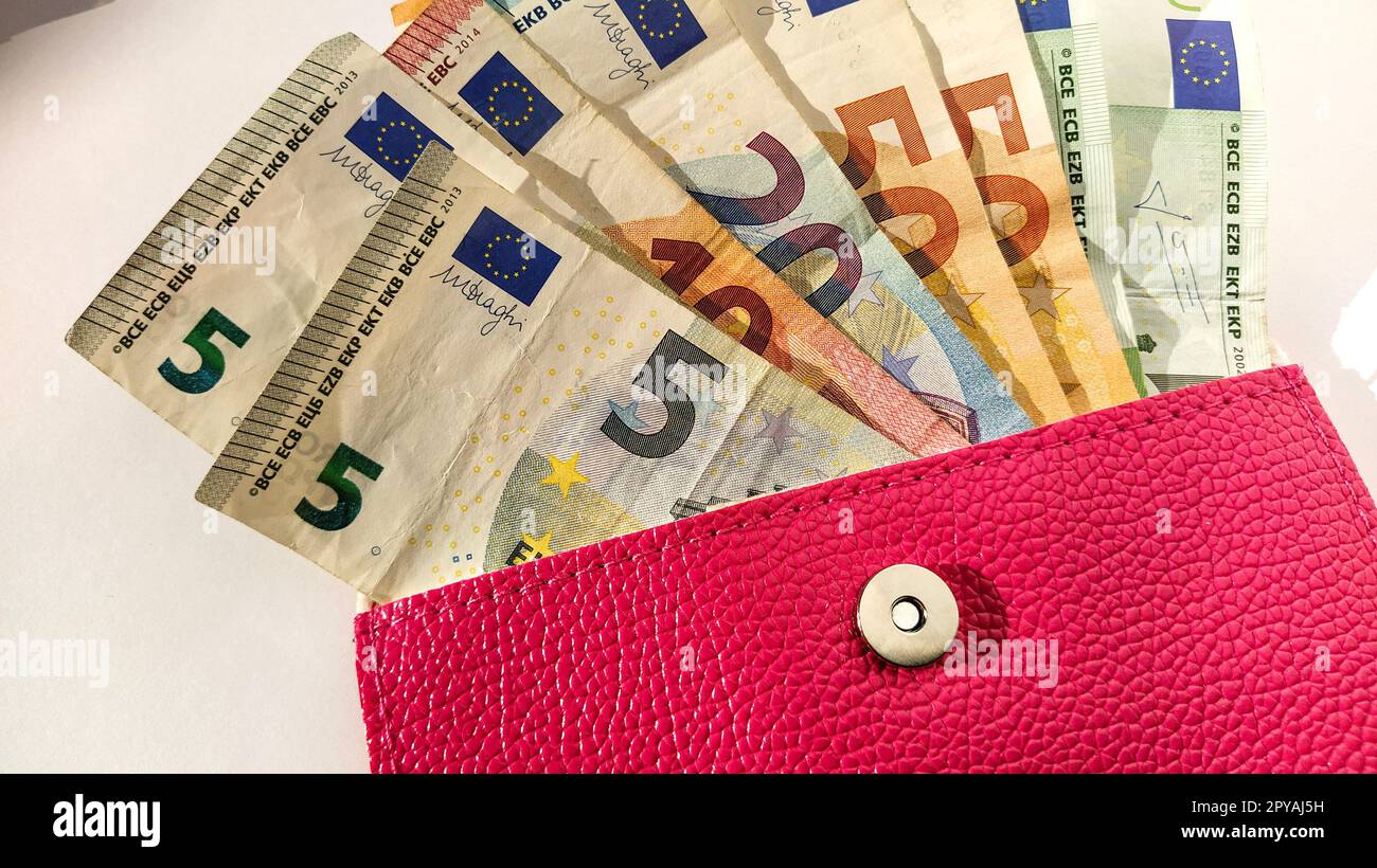Euro-Papiernoten. Europäische Währung auf weißem Hintergrund. Eine Handtasche oder Handtasche in leuchtendem Rosa mit einem Metallknopf, aus der das Geld in einem Fächer verteilt wird. Banknoten von 5, 10, 20, 50 und 100 Stockfoto