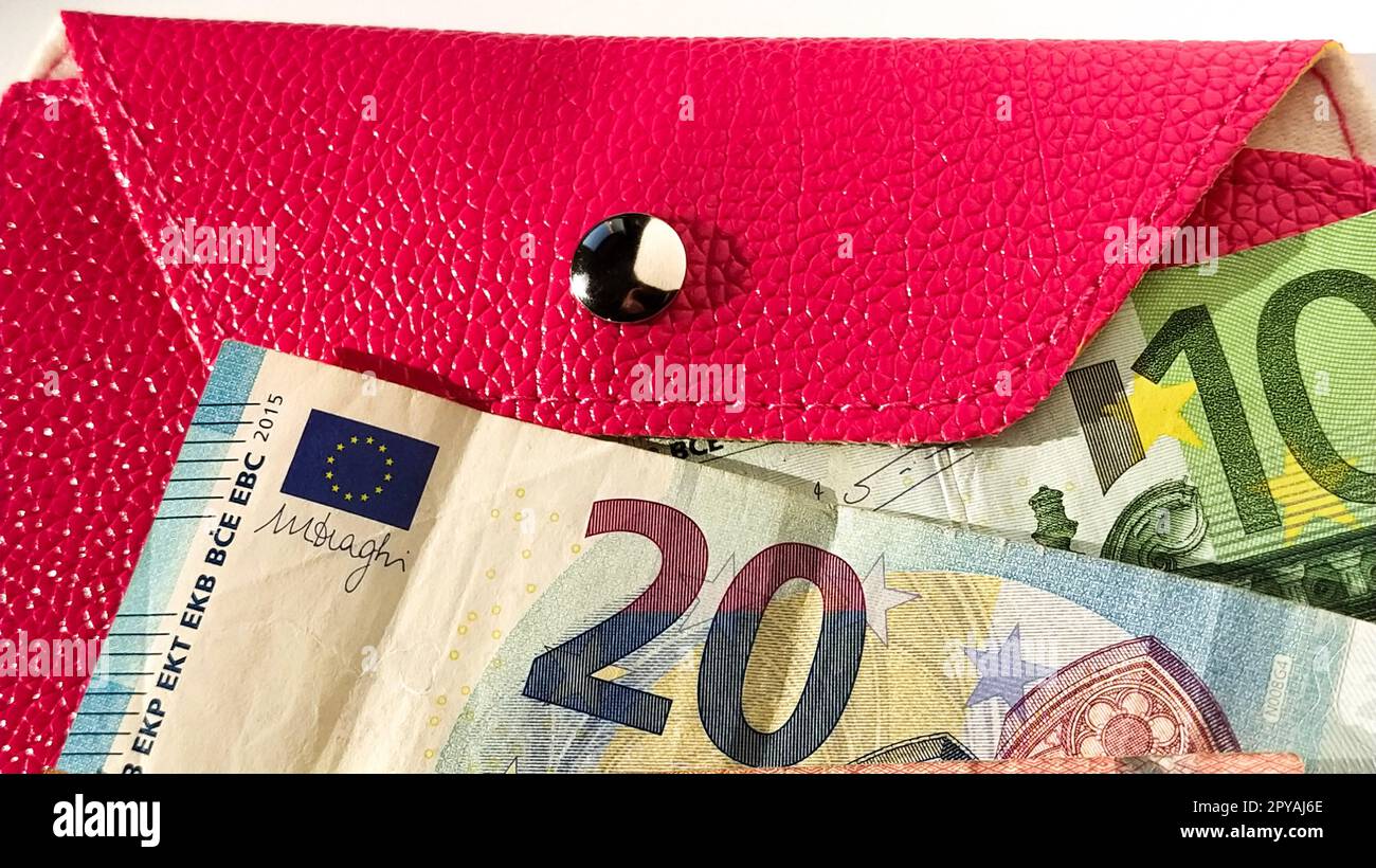 Euro-Papiernoten. Europäische Währung auf weißem Hintergrund. Geldbörse oder Handtasche in leuchtendem Pink mit einem glänzenden metallischen Knopf. Banknoten der Zentralbank für 20 und 100 Euro Stockfoto