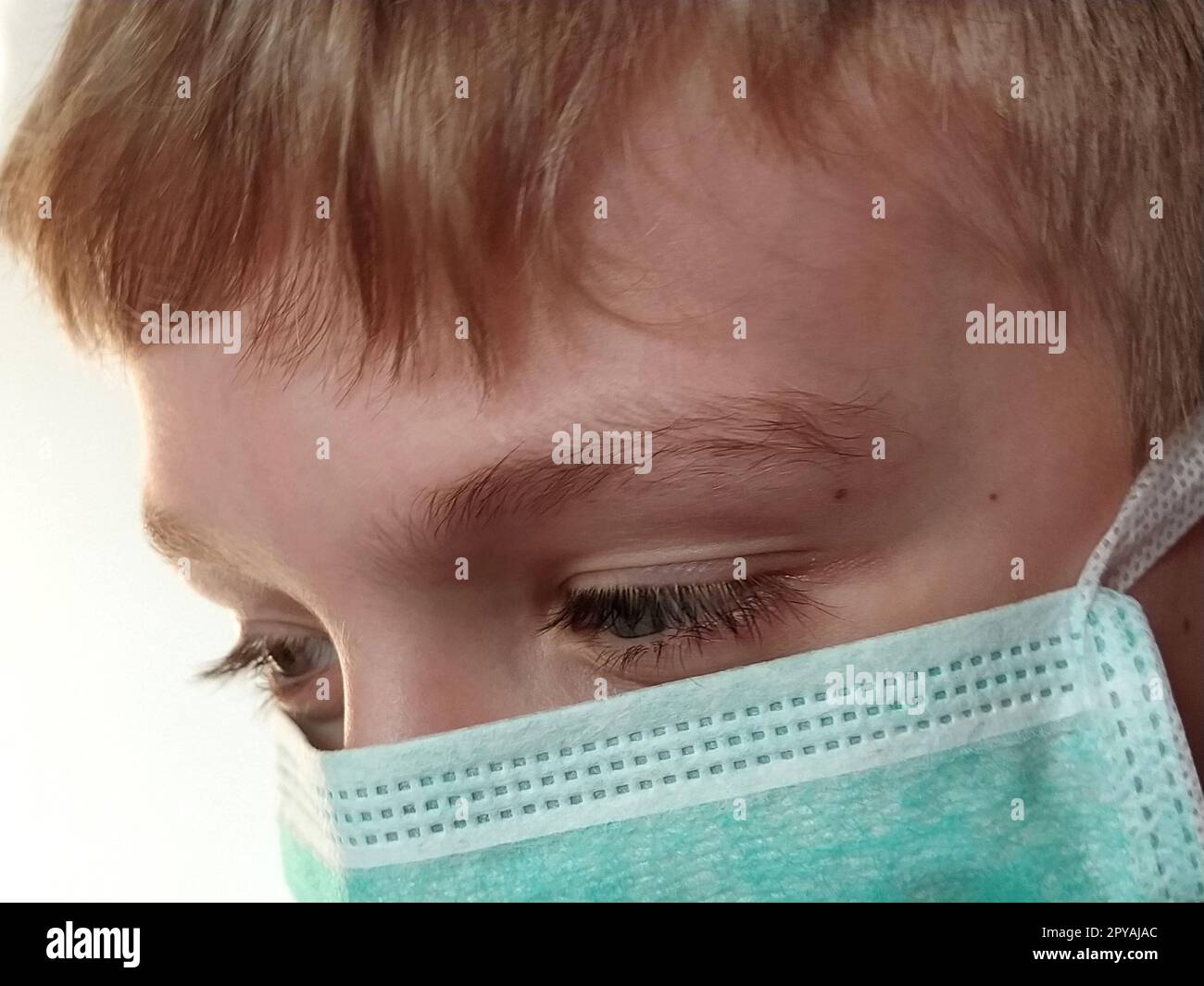 Maskiertes Kind. Das Gesicht eines 7-jährigen Jungen in einer schützenden Operationsmaske. Schuljunge mit blonden Haaren und blaugrauen Augen auf weißem Hintergrund Stockfoto