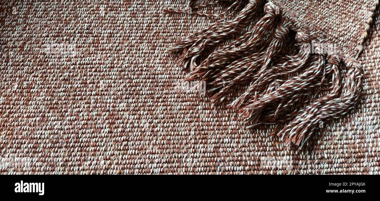 Gewebter Stoff mit Quasten. Grobe Weben von Baumwolle. Bodenmatte. Beige, weiße und zerknitterte Fäden beim Weben. Wolle oder Acryl. Stockfoto