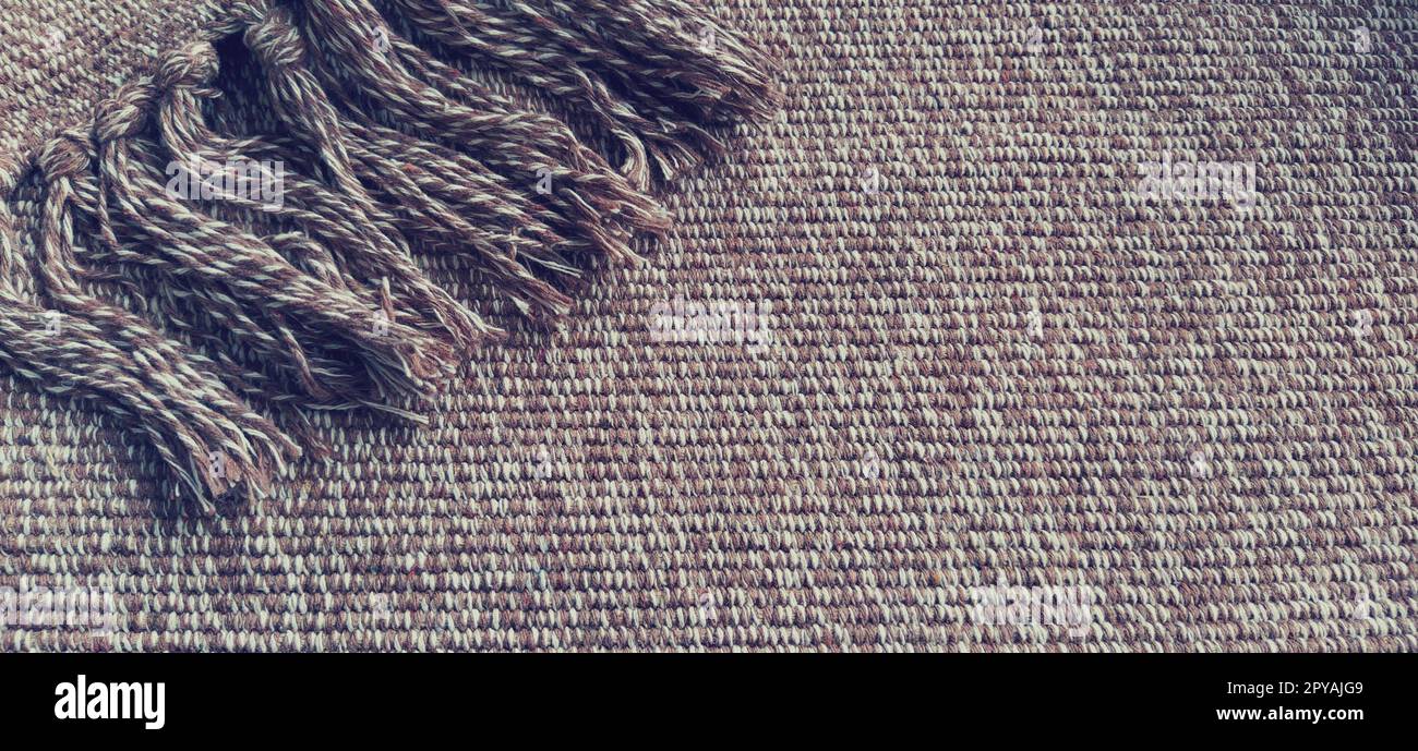 Gewebter Stoff mit Quasten. Grobe Weben von Baumwolle. Bodenmatte. Beige, weiße und zerknitterte Fäden beim Weben. Wolle oder Acryl. Stockfoto