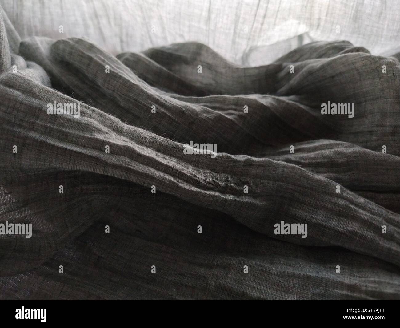 Lichtdurchlässige Vorhänge oder Tüll im skandinavischen Stil. Grauer Plisseestoff oder zerknitterter Stoff hängen nach unten. Nahaufnahme. Die untere Kante des Vorhangs liegt auf einer horizontalen Fläche. Weichzeichner. Stockfoto