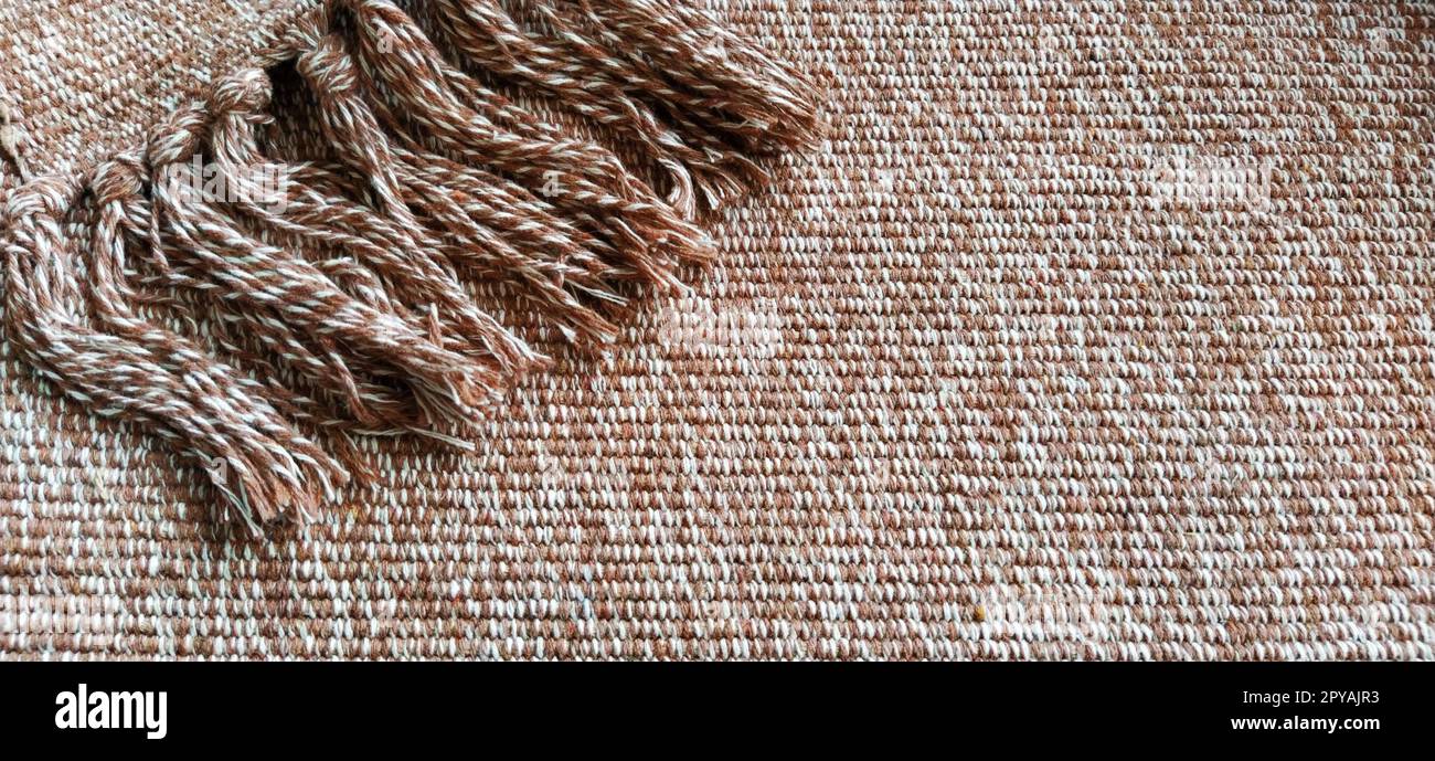 Gewebter Stoff mit Quasten. Grobe Weben von Baumwolle. Bodenmatte. Beige, weiße und zerknitterte Fäden beim Weben. Wolle oder Acryl Stockfoto