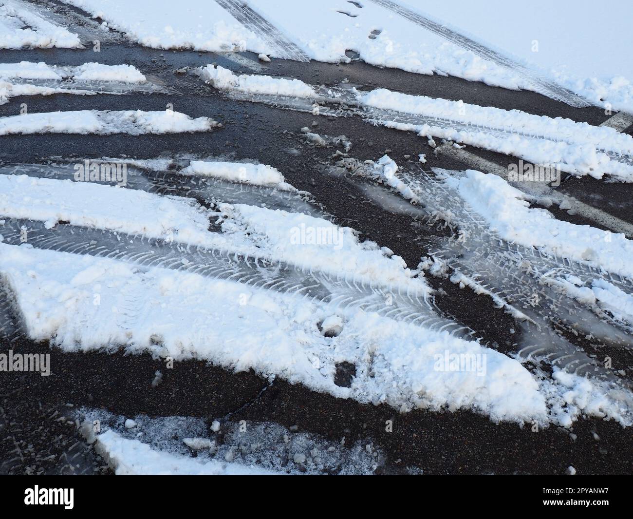 Schneeverwehungen am Straßenrand. Schlechtes Wetter und Verkehr. Schnee auf Asphalt. Schwierige Fahrbedingungen. Winterschlamm auf der Straße. Bremsweg eines Autos. Stockfoto