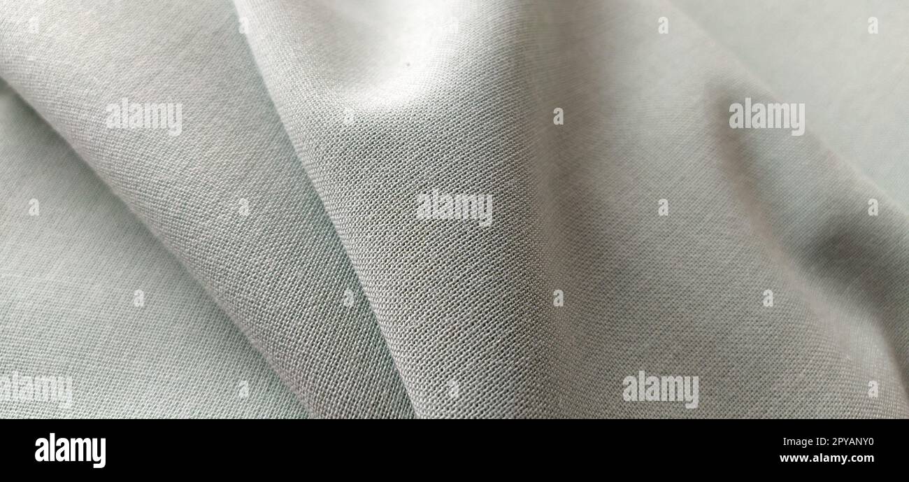 Weißes Material mit Nahaufnahme der verflochtenen Fäden. Hellgrüner Farbton. Schöne Wellen auf dem Material. Ein ordentlich gefaltetes Stück Stoff. Innendekoration, Schneiderei. Textilindustrie Stockfoto