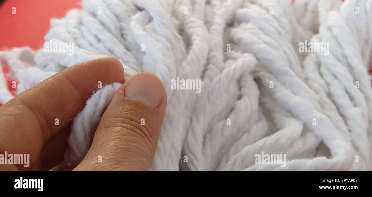 Die Hand einer Frau berührt die Baumwollfäden des Moppkopfes. Auswahl eines Mopps für die Reinigung. Haushaltsreinigungsarbeiten. Weiße Seile. Die Finger der Putzfrau. Stockfoto