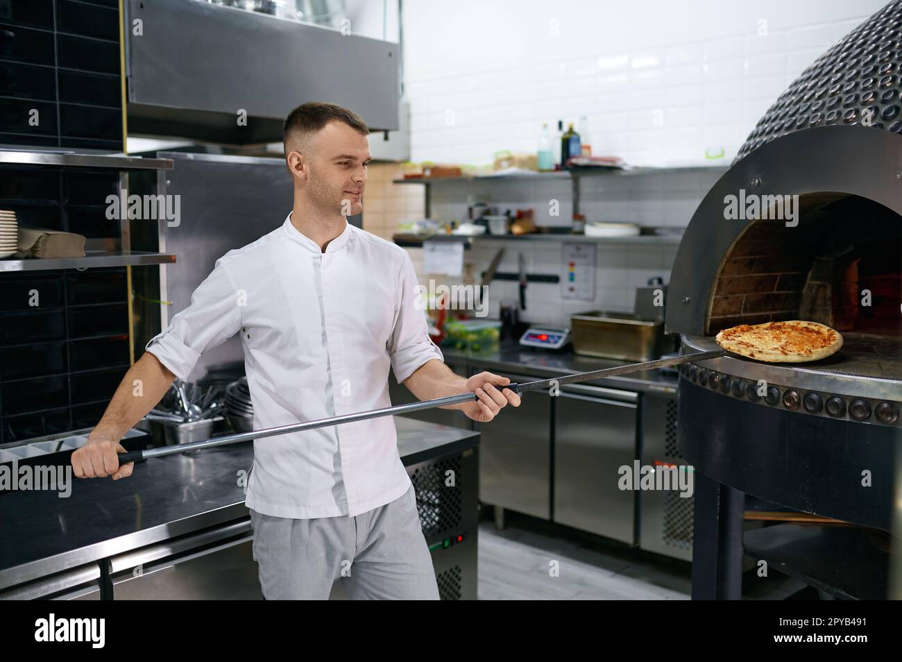 Junger männlicher Koch mit frisch gebackener Pizza auf langer Schaufel, selektiver Fokus Stockfoto