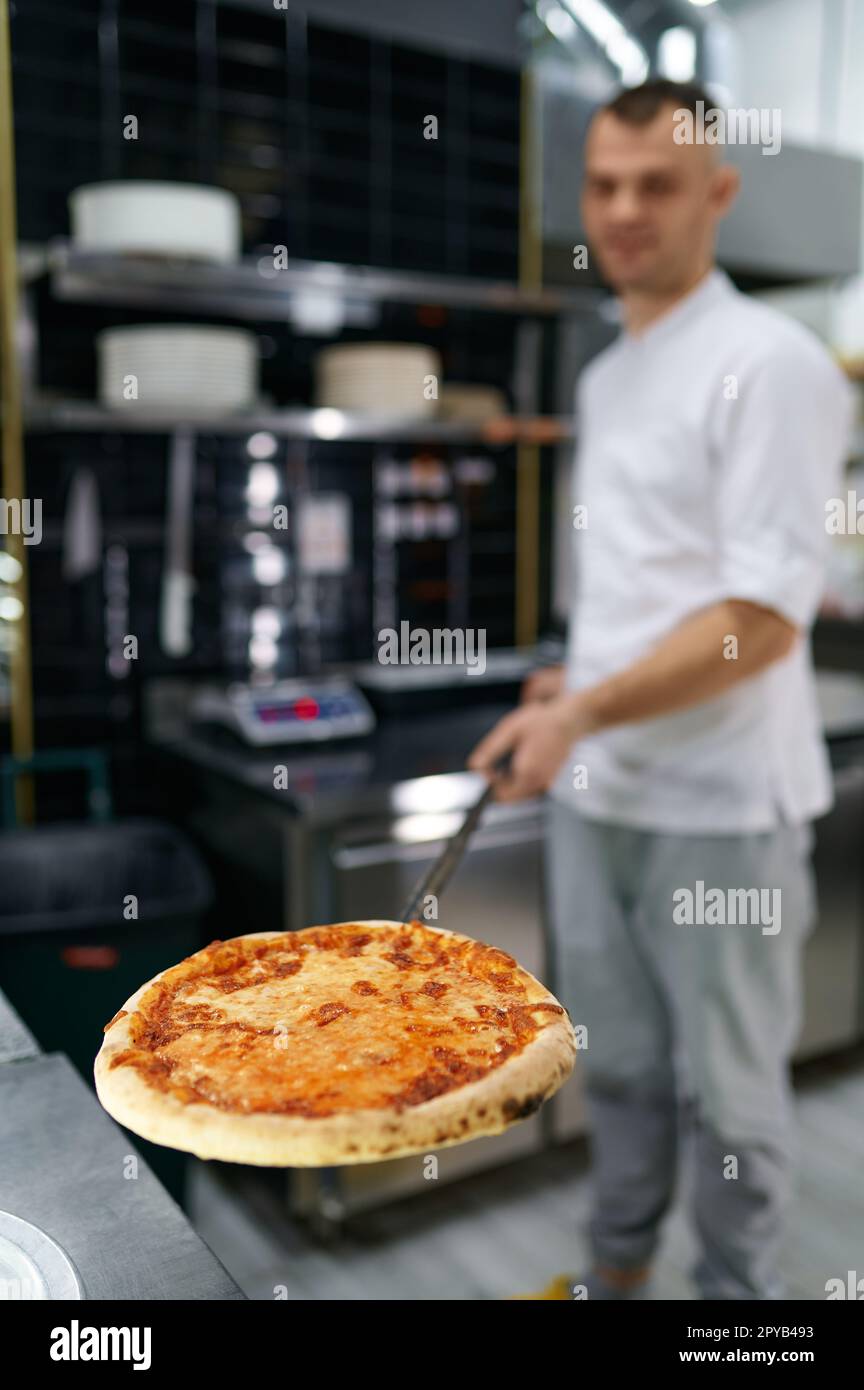 Junger männlicher Koch mit frisch gebackener Pizza auf langer Schaufel, selektiver Fokus Stockfoto