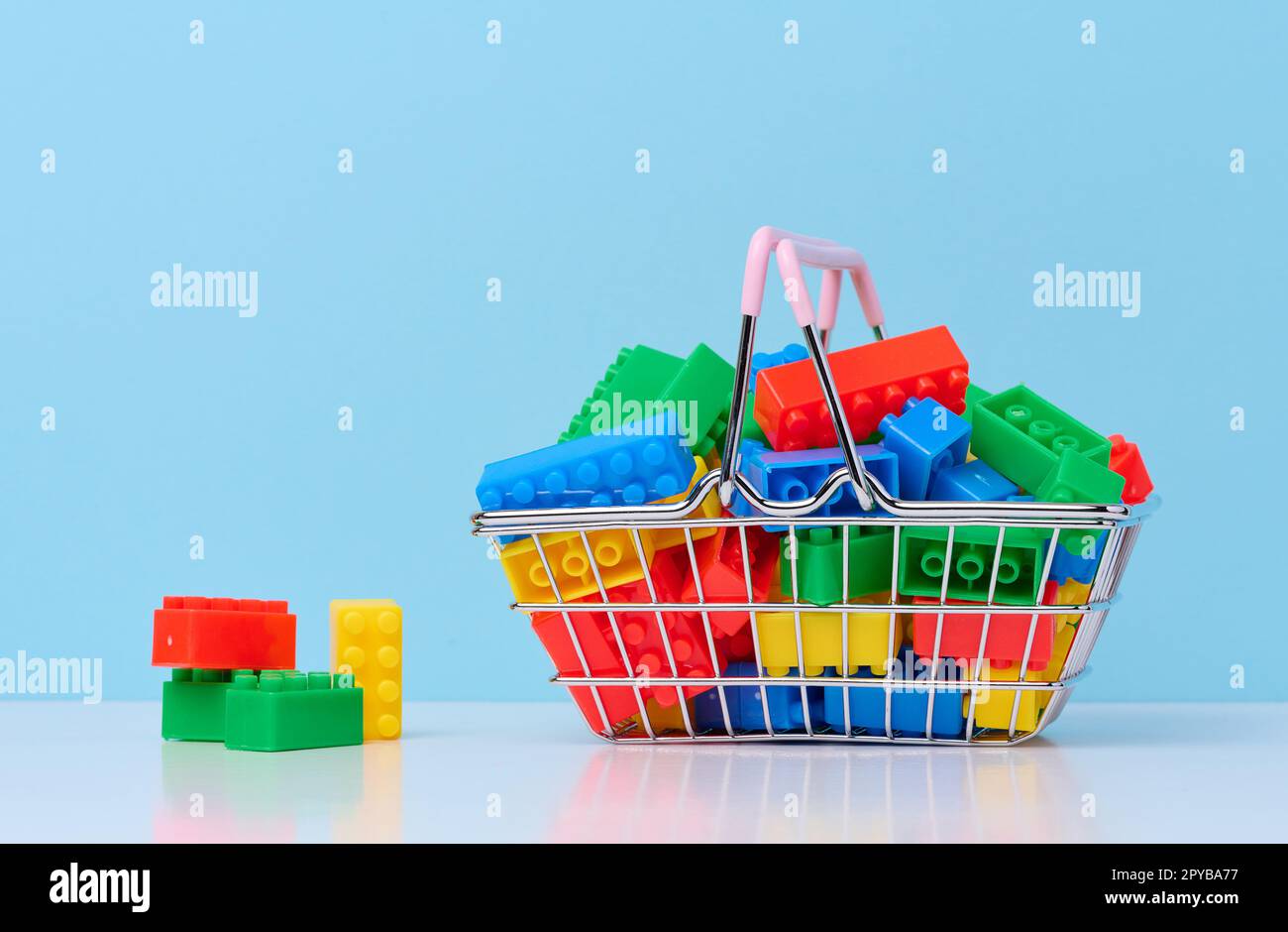 Farbenfrohe Kunststoffbausteine in einem Miniatur-Einkaufswagen aus Metall, pädagogisches Spiel für Kinder Stockfoto