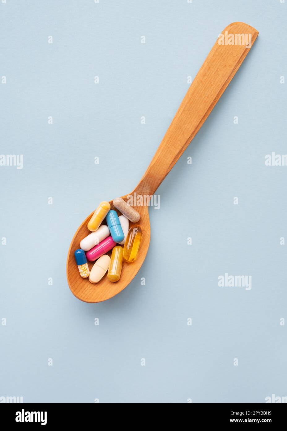 Verschiedene helle Pillen auf blauem Hintergrund liegen in einem Holzlöffel. Das Konzept der Gesundheitsversorgung und evidenzbasierten Medizin, Nahaufnahme. Stockfoto