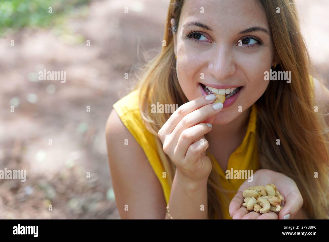 Ein wunderschönes, gesundes Mädchen, das Cashew-Nüsse im Park isst. Schaut zur Seite. Stockfoto