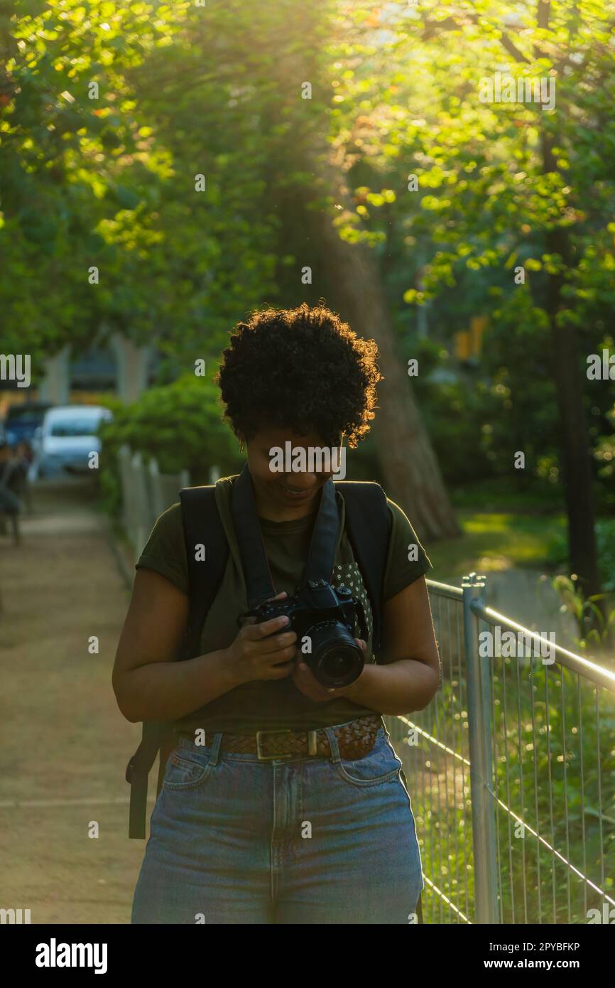 Glückliche junge afroamerikanische Fotojournalistin mit dunklen lockigen Haaren, erstaunt und zufrieden mit offenem Mund das Ergebnis der Fotos Stockfoto