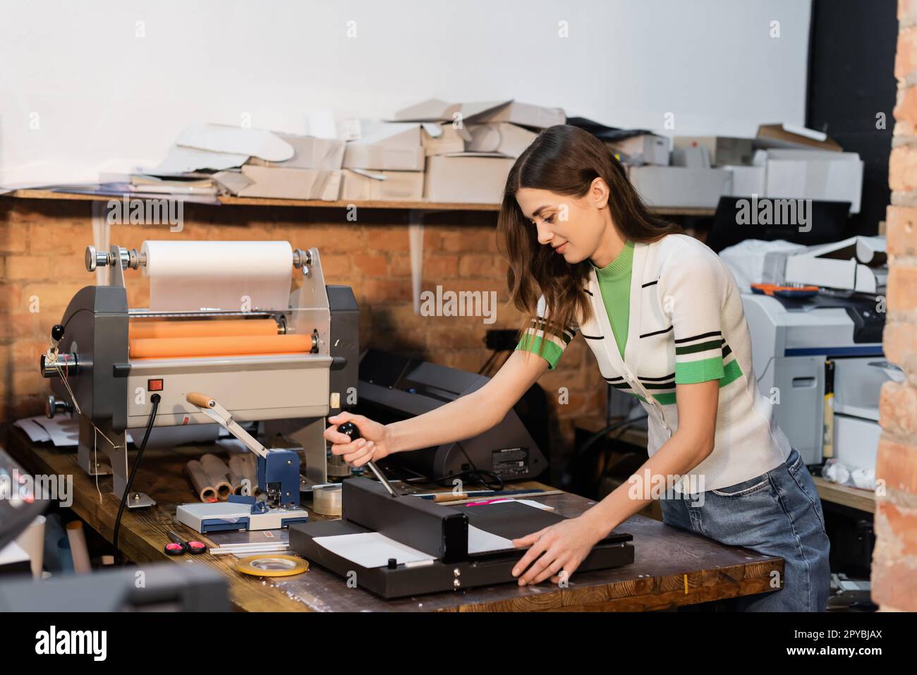 Fröhlicher Typograph, der den Papierschneider neben dem Plotter im Print Center benutzt, Bild aufzeichnen Stockfoto