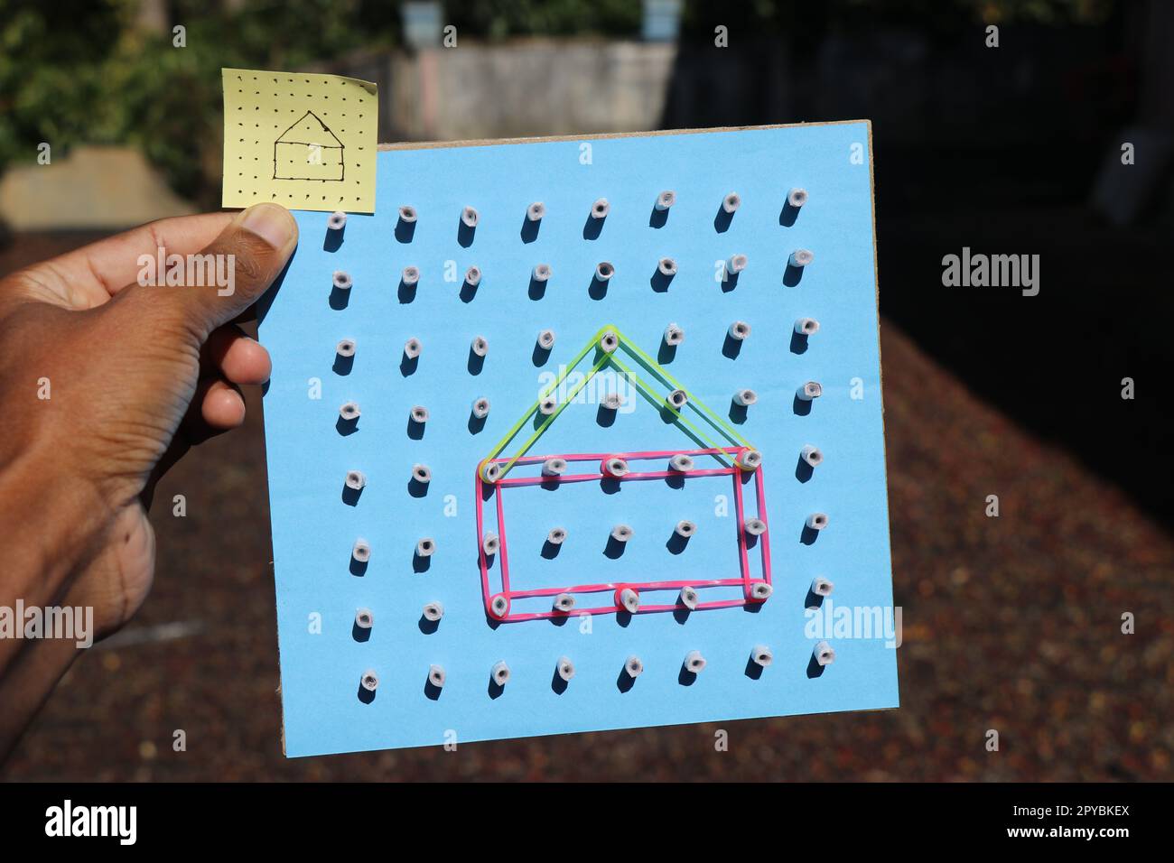 Geoboard aus Pappe zu Hause mit einem Bild des Zeichnens, das mit einem elastischen Band in der Hand gemacht wurde. Pädagogisches Spielzeug aus recycelten Materialien Stockfoto