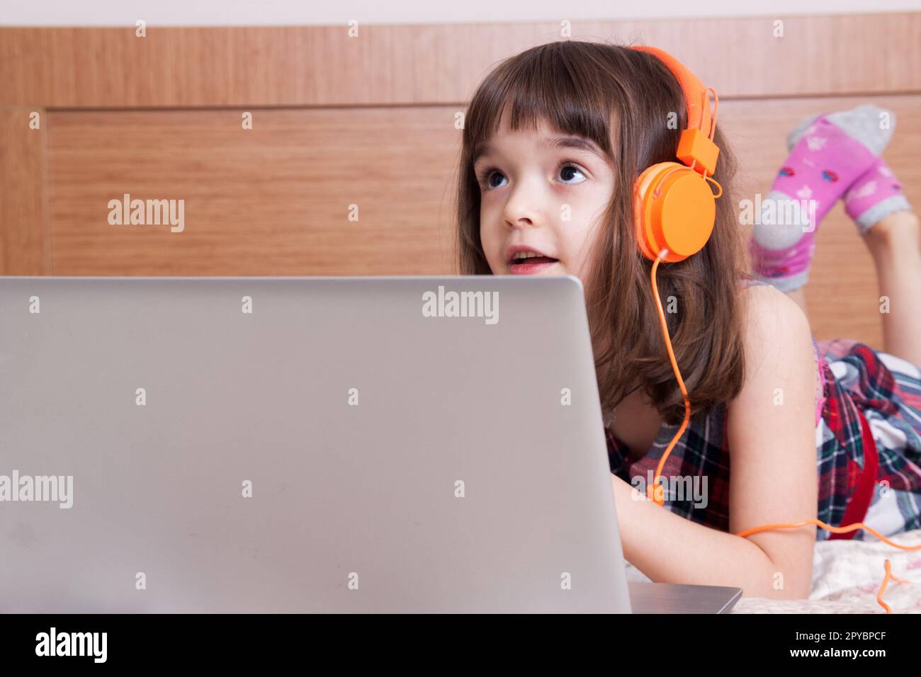 Kleines Mädchen, das den Laptop mit Ohrhörern benutzt Stockfoto