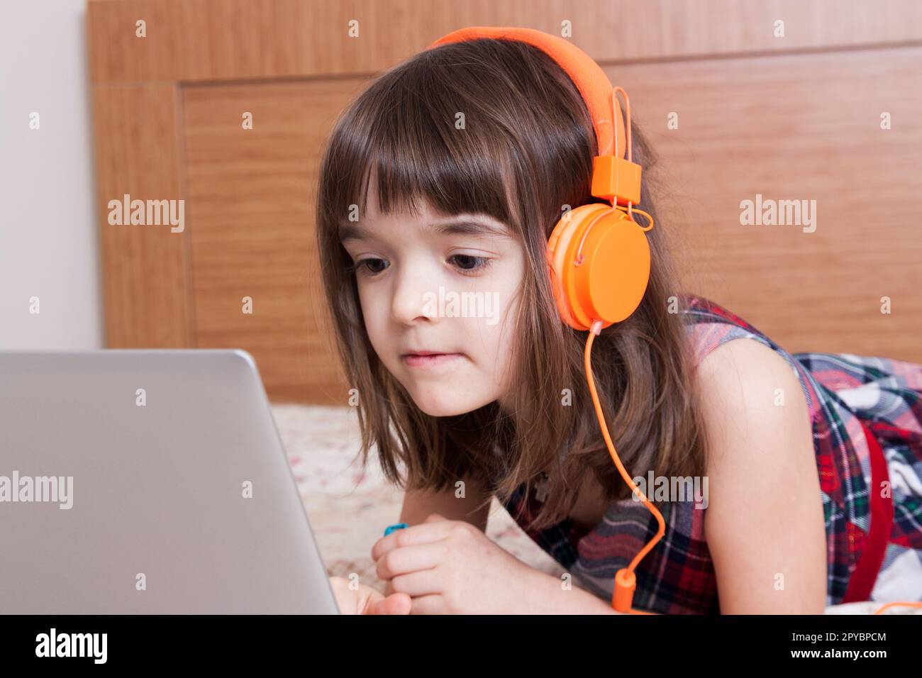 Kleines Mädchen, das den Laptop mit Ohrhörern benutzt Stockfoto