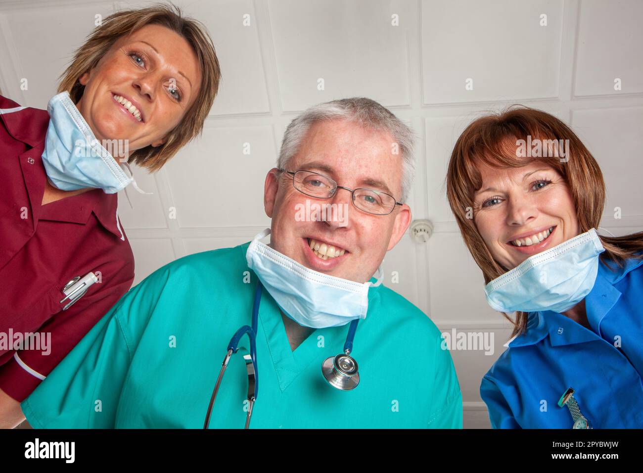 Angehörige Der Heilberufe: Das Bewusstsein Wiedererlangen. Ein lächelndes uniformiertes medizinisches Team, das auf ihren erwachenden Patienten hinunterblickt. Aus einer Reihe von zugehörigen Bildern. Stockfoto