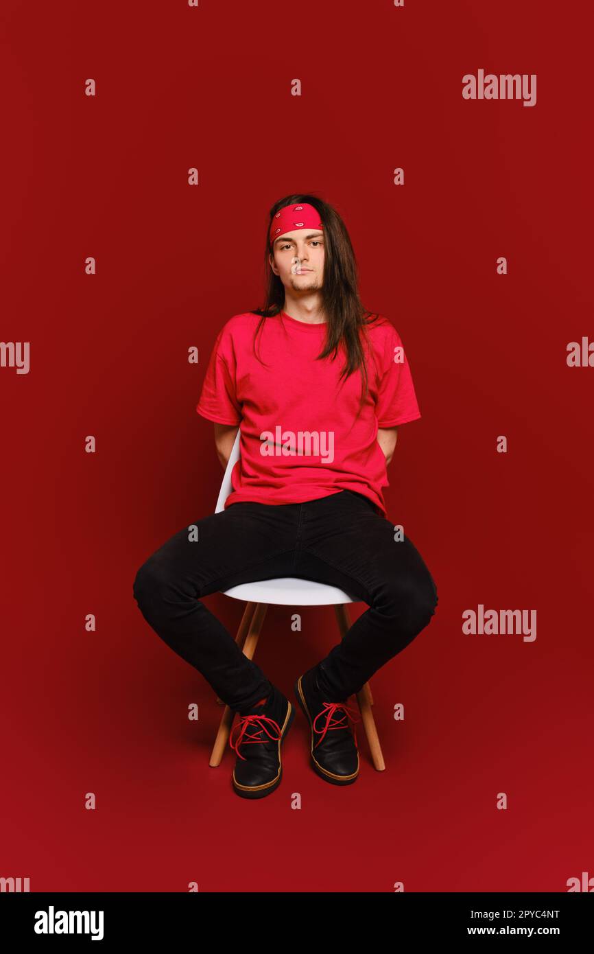 Ein junger Mann in schwarz-roter Freizeitkleidung sitzt auf einem Stuhl mit den Armen hinter dem Rücken Stockfoto