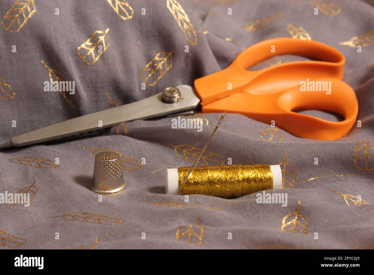 Spule mit Gewinde in Metallic Gold auf grauem und goldenem Stoff Stockfoto