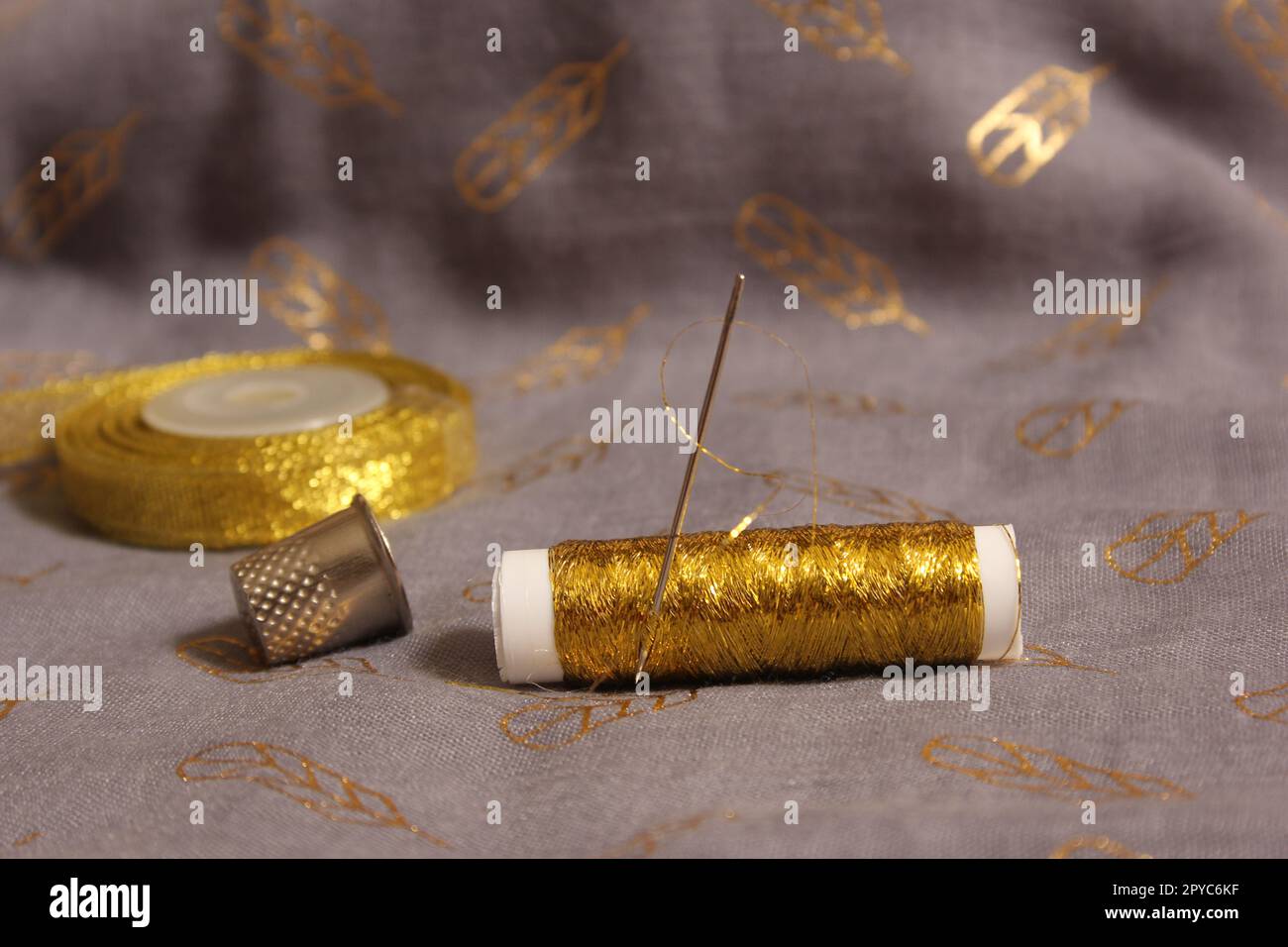 Spule mit Gewinde in Metallic Gold auf grauem und goldenem Stoff Stockfoto