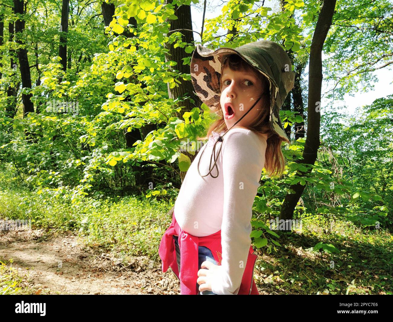 Hübsches Mädchen, 6 Jahre alt, mit Jagdhut, macht sich ein Grimace im Gesicht. Gefühl der Überraschung, Angst oder Entmutigung. Das Kind dreht sich um und schaut in die Kamera. Wald im Hintergrund Stockfoto