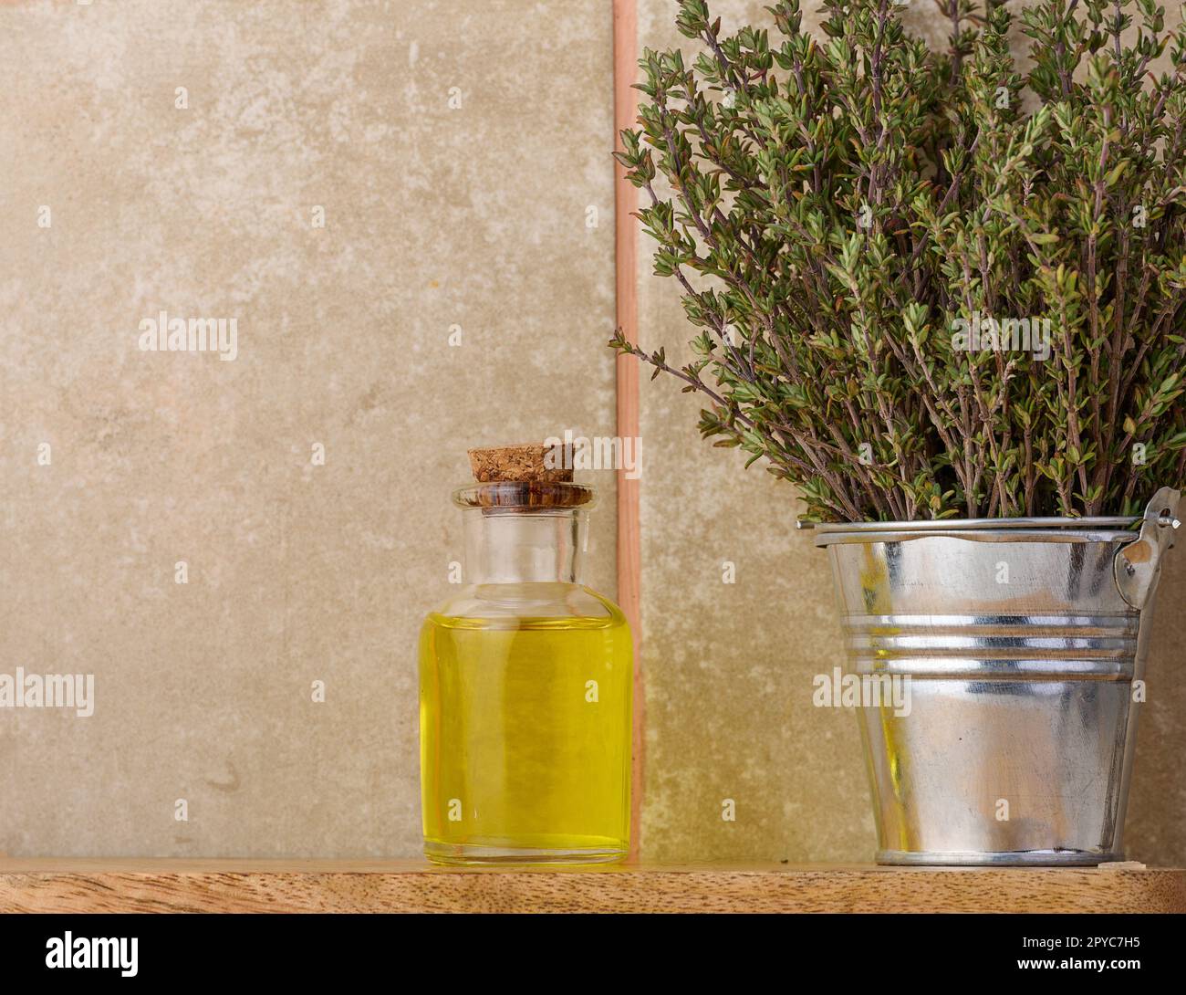 Eine durchsichtige Glasflasche mit Öl und frischen Thymianzweigen in einem Miniatureimer auf einem Holztisch, kosmetisches Behandlungsöl. Stockfoto