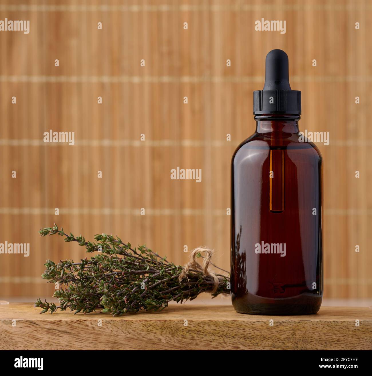 Ätherisches Thymianöl in Glasflasche mit Tropfer und frischen Thymianzweigen auf dem Tisch, kosmetische Zutat Stockfoto