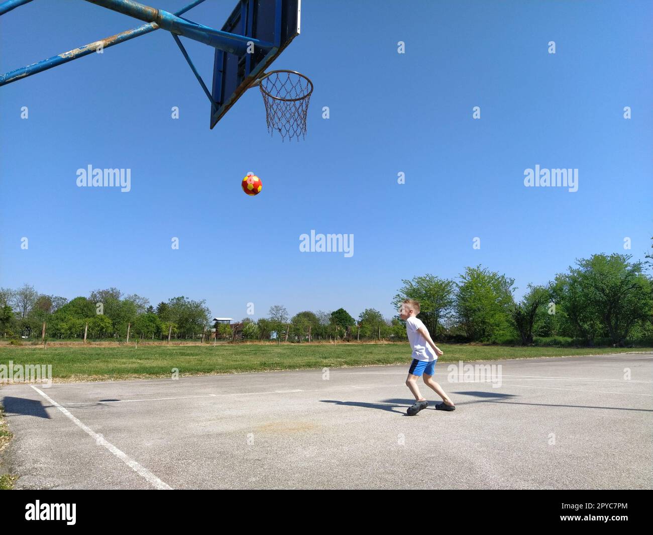 Sremska Mitrovica, Serbien. 6. Juni 2020. Ein Junge spielt Ball auf dem Spielplatz. Asphaltsportplatz. Ein Kind in einem weißen T-Shirt. Kleinkind mit blondem Haar, 7 Jahre alt. Laufen, Treten und Übungen Stockfoto