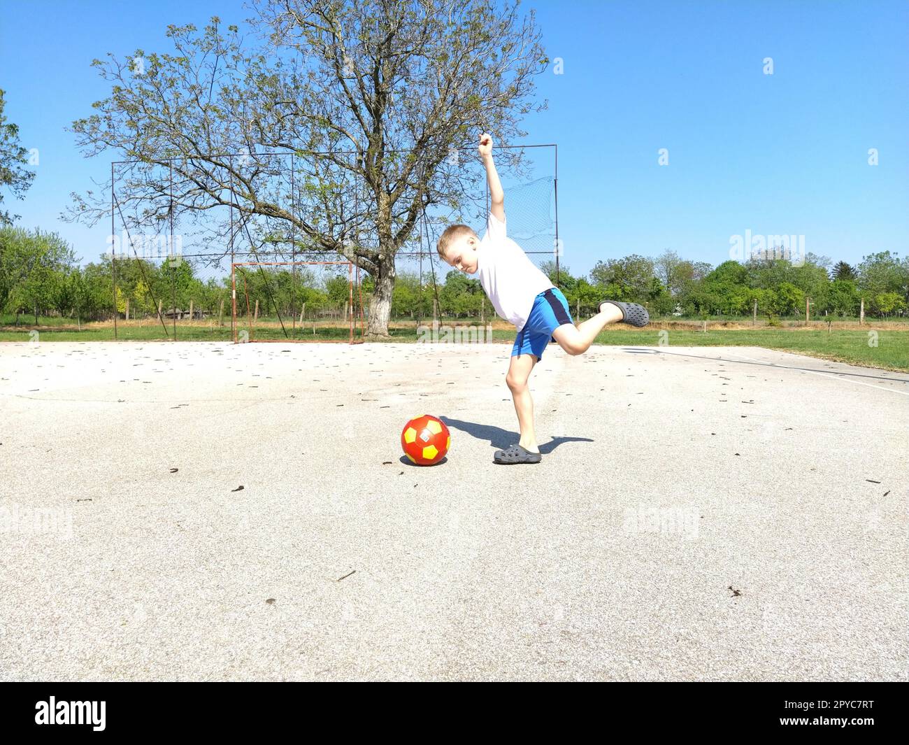 Sremska Mitrovica, Serbien. 6. Juni 2020. Ein Junge spielt Ball auf dem Spielplatz. Asphaltsportplatz. Ein Kind in einem weißen T-Shirt. Kleinkind mit blondem Haar, 7 Jahre alt. Laufen, Treten und Übungen Stockfoto