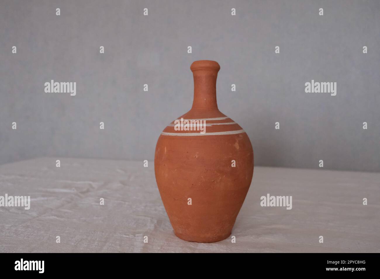 Vorderansicht eines alten unlackierten antiken Keramikkastens auf einer weißen Tischdecke. Tonkrug zum Trinken von Wein oder Wasser. Stockfoto