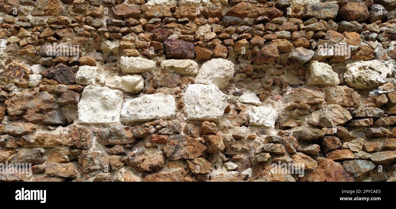 Steinmauer. Gestapelte große Ziegel und Kopfsteinpflaster in warmen Farben. Lose weiße Steine, die aus der Wandoberfläche hervorstehen. Turm in Vrdnik, Serbien. Stockfoto