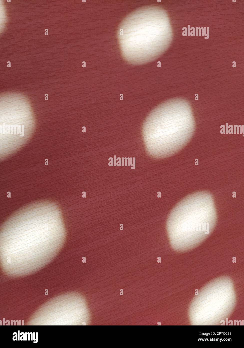 Roter Hintergrund mit Punkten. Sonnenstrahlen, die durch die Löcher in den Jalousien scheinen und die leicht verschwommene Kreise auf die farbige Oberfläche malen Stockfoto