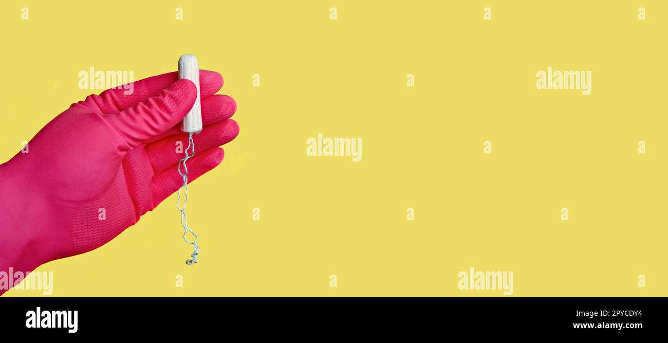 Frau trägt einen rosa Handschuh und hält einen Baumwoll-Tampon vor gelbem Hintergrund. Stockfoto