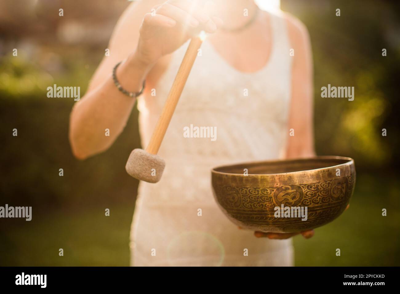 Frau spielt tibetische Bowl mit Hammer über Sunset Sky. Entspannende Musiktherapie und Sound Healing. Friedliches Meditations- und Entspannungskonzept. Stockfoto