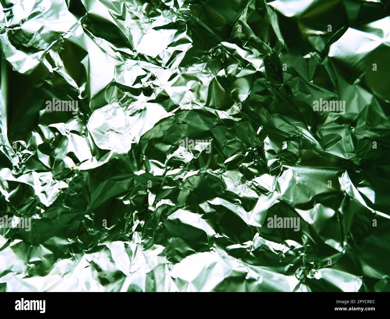 Nahaufnahme der Folie. Zerknitterte Aluminiumfolie. Abstrakter metallischer Hintergrund. Folie zum Backen von Speisen. Hintergrund mit grünem Farbton Stockfoto