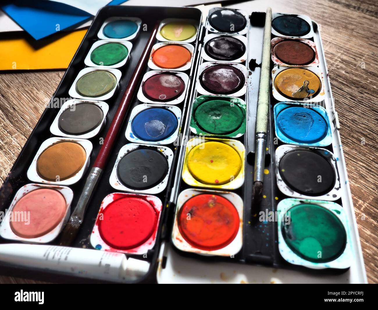 Ein Satz von Wasserfarben in verschiedenen Farben für das Zeichnen. Mehrfarbige runde Behälter mit heller Farbe. Werkzeuge für den Unterricht von Zeichnen und Arbeit. Farbiges Papier. Rot, Blau, Gelb, Grün. Stockfoto