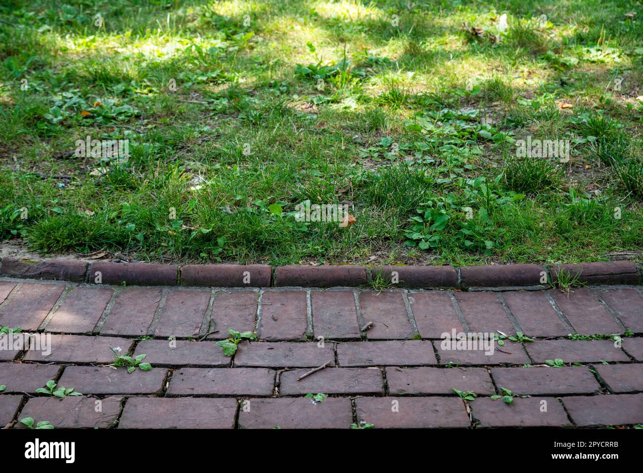 Kolonialer roter Backsteinweg und grüner Rasen im Hintergrund Stockfoto