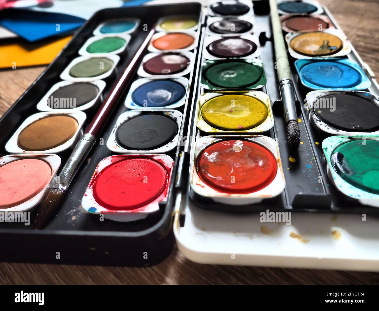 Ein Satz von Wasserfarben in verschiedenen Farben für das Zeichnen. Mehrfarbige runde Behälter mit heller Farbe. Werkzeuge für den Unterricht von Zeichnen und Arbeit. Farbiges Papier. Rot, Blau, Gelb, Grün. Stockfoto