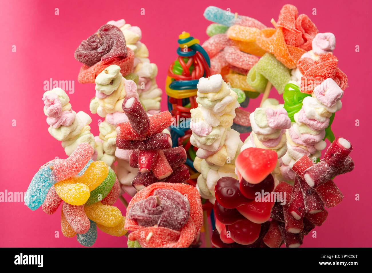 Auswahl an bunten Fruchtgummi Süßigkeiten spießten saure Gummibären auf Holzspießen, isoliert auf magentarotem Hintergrund Stockfoto