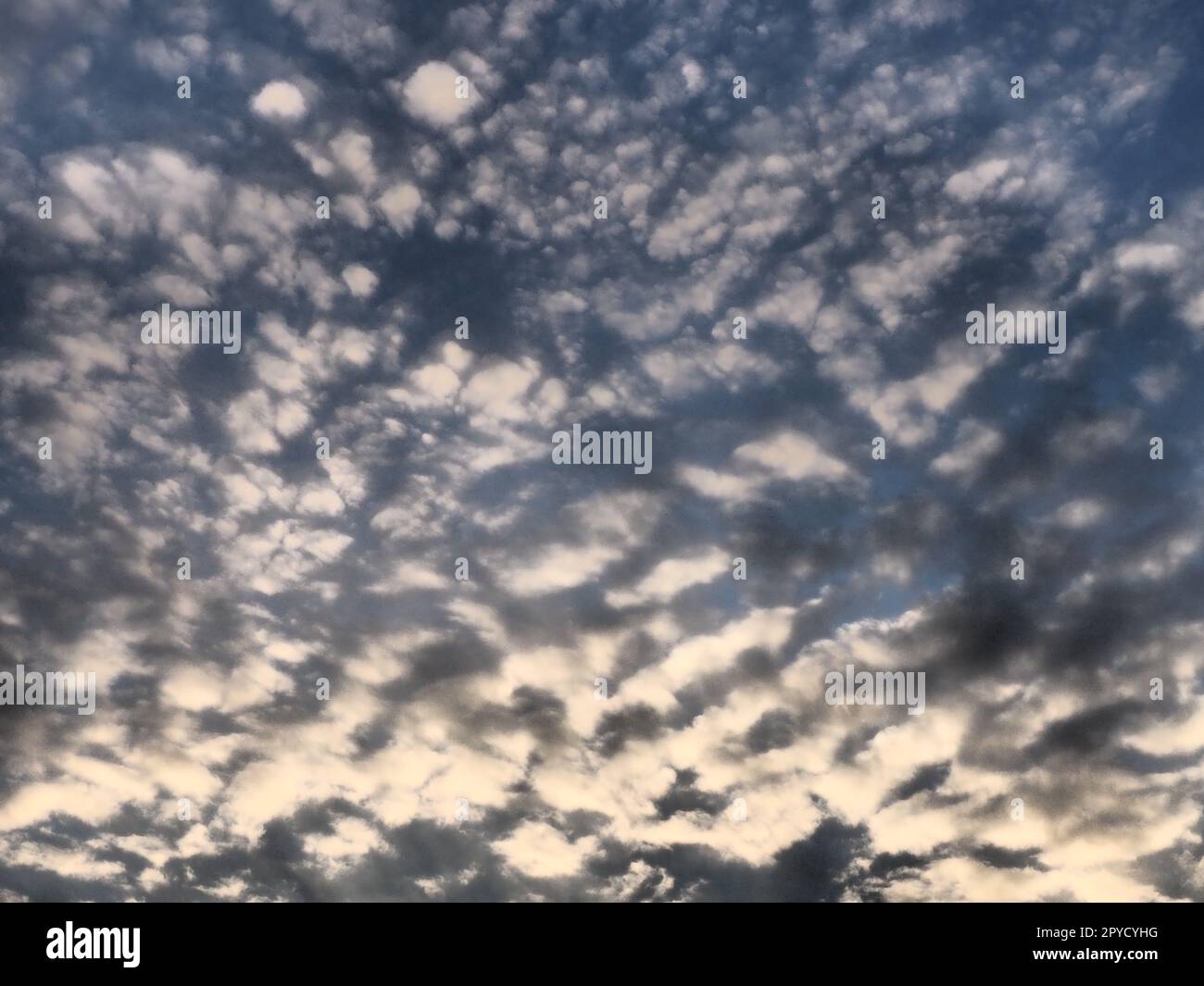 Wolken am Abendhimmel. Die Sonnenstrahlen durchdringen die Wolken. Blaue, gelbe und orangefarbene Farben des Himmels und der Wolken. Wunderschöne Landschaft. Die Sonne geht unter Stockfoto