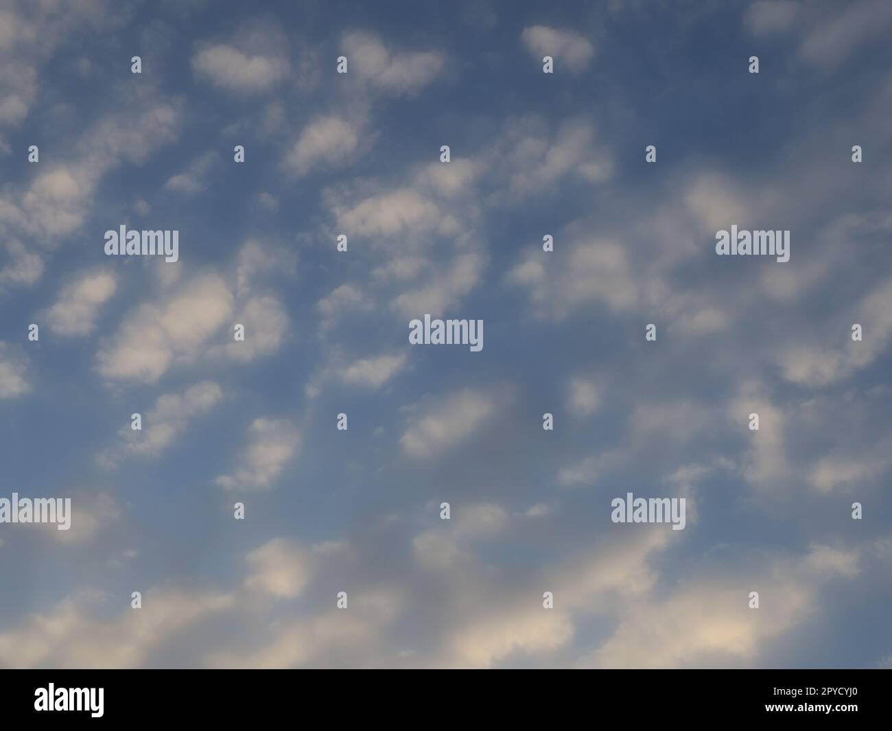 Wolken am Abendhimmel. Die Sonnenstrahlen durchdringen die Wolken. Blaue, gelbe und orangefarbene Farben des Himmels und der Wolken. Wunderschöne Landschaft. Die Sonne geht unter Stockfoto