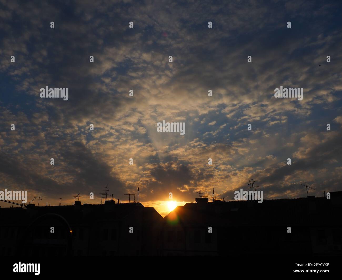 Wolken am Abendhimmel. Die Sonnenstrahlen durchdringen die Wolken. Blaue, gelbe und orangefarbene Farben des Himmels und der Wolken. Wunderschöne Landschaft. Die Sonne geht unter Stockfoto