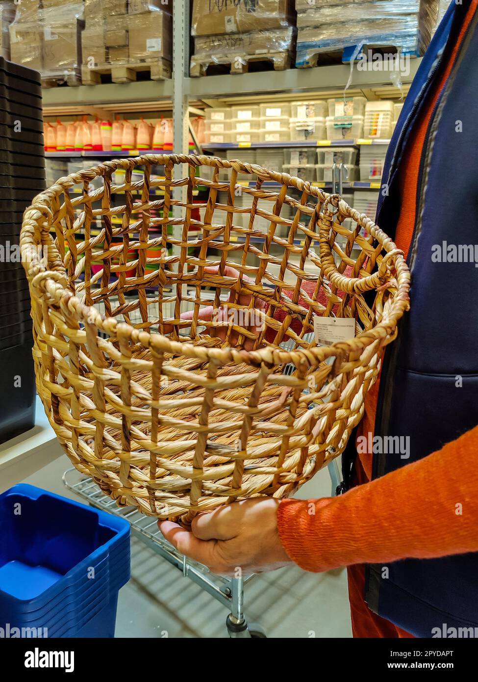 Ein Mann in einem orangefarbenen Pullover und einer blauen Weste hält einen Korb in den Händen. Auswahl an Waren im Supermarkt. Nahaufnahme. Selektiver Fokus. Stockfoto