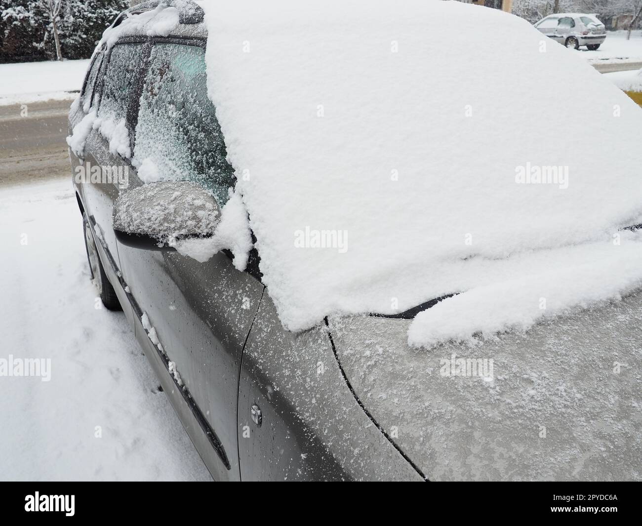 Schnee und Eis auf der Windschutzscheibe, den Rückspiegeln des Fahrzeugs. Winterliche Fahrbedingungen. Schneeräumen. Strassenverkehr im Winter. Metallic-Auto. Schneewehen und Matsch. Stockfoto